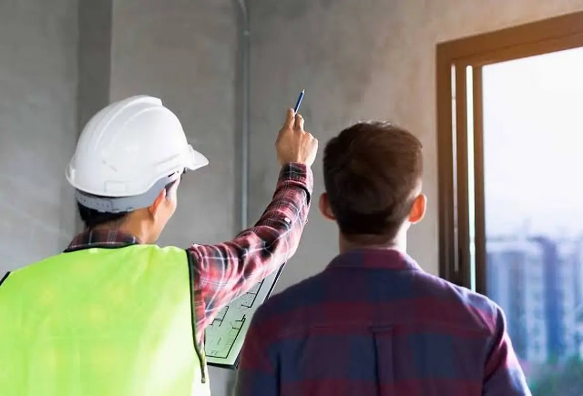 A site engineer in a hard hat pointing out details to a homeowner beside a window