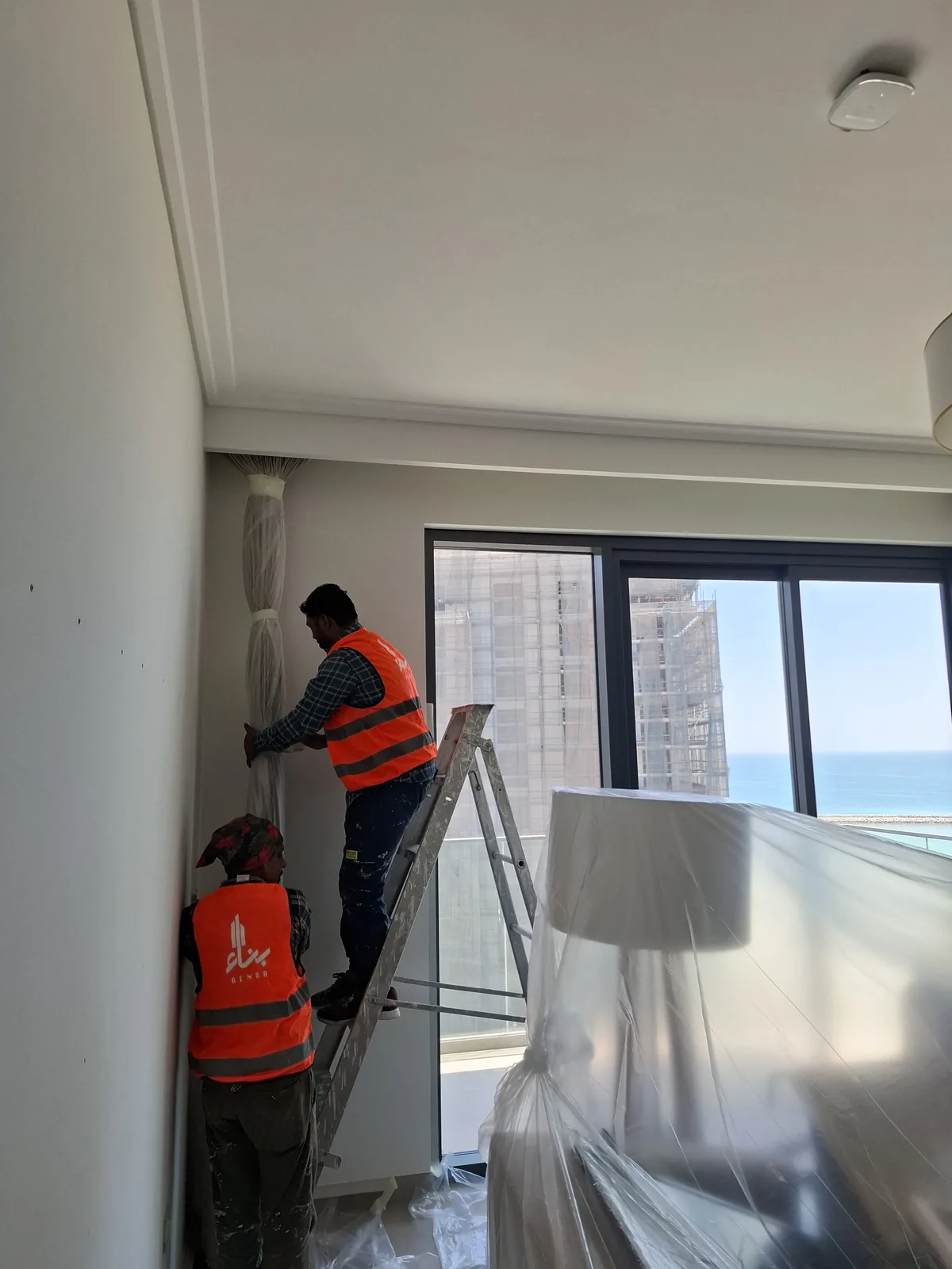 Benaa Contracting painters preparing walls in a private flat at Marassi, with furniture sheeted for protection