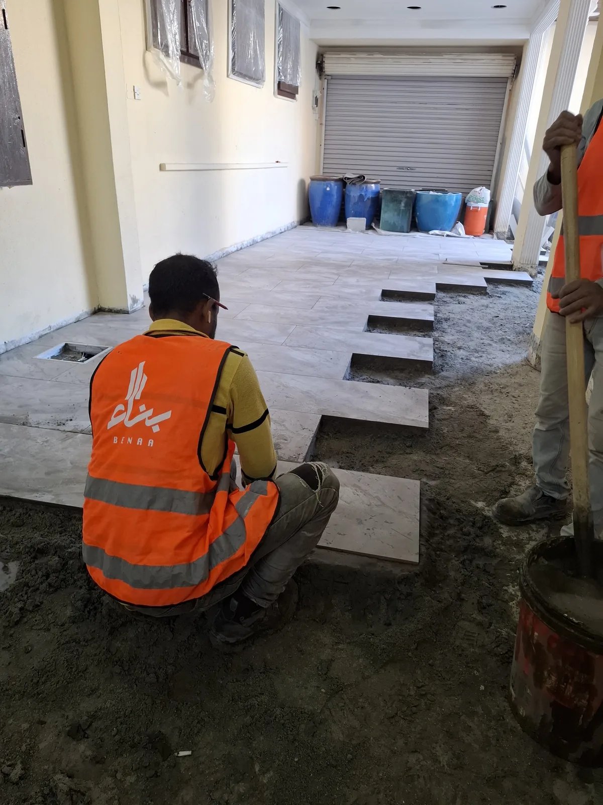 Benaa Contracting tiler in a branded vest laying large porcelain tiles onto a screed bed